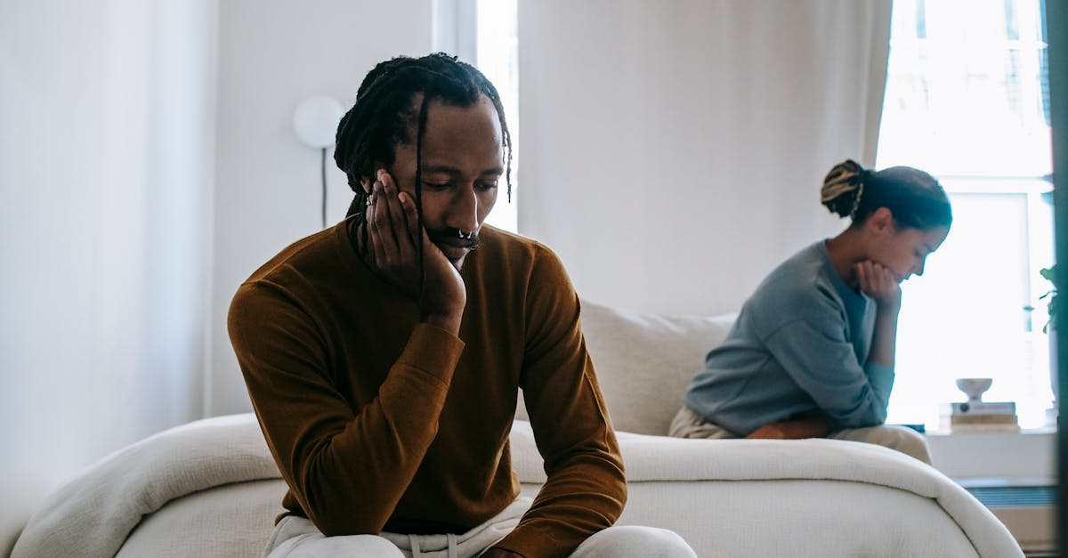 A couple sits thoughtfully on a bed at home, reflecting on their relationship.